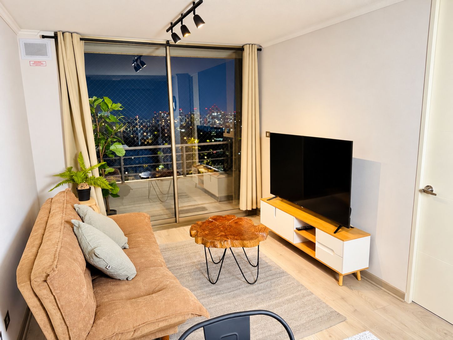 A modern living room with a sofa, a television, and a balcony with a city view.