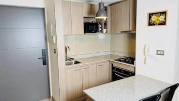 A compact kitchen with a grey door, wooden cabinets, a microwave, a sink, and a small dining area with a table and chairs.