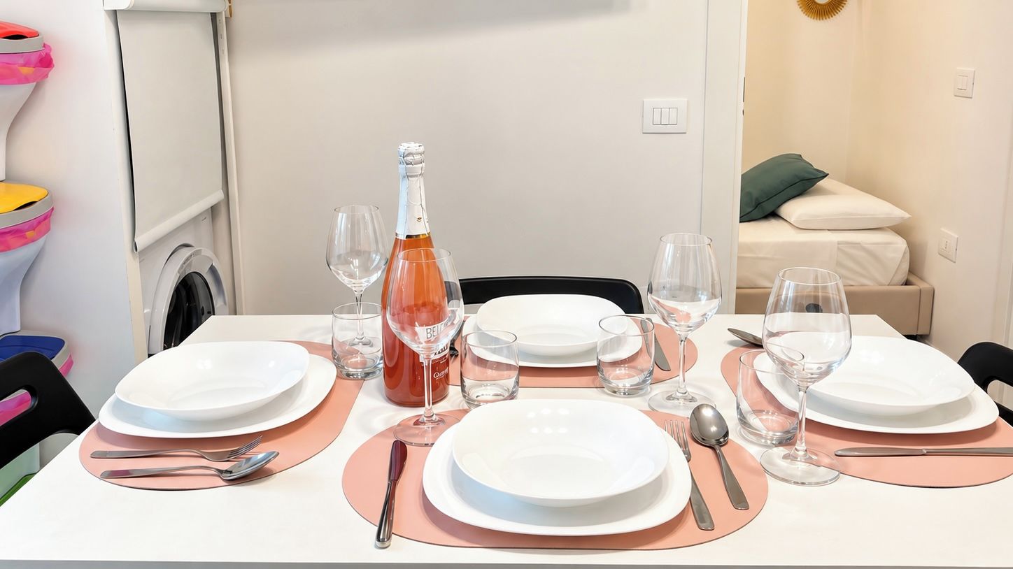 A dining table set with plates, cutlery, and wine glasses, with a bottle of wine in the center.