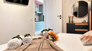 A hotel room with a bed, a bedside table with a vase of flowers, and a door leading to a bathroom.