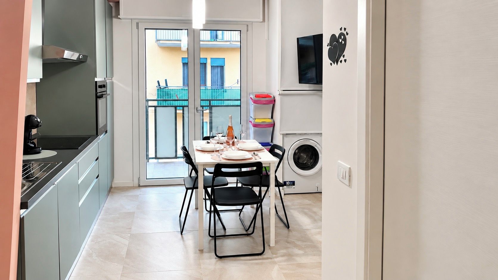 A compact kitchen with a dining area, a washing machine, and a view of the outside balcony.