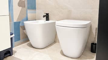 A modern bathroom with two white toilets, a black faucet, and a trash bin.