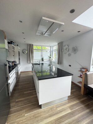 A modern kitchen with a central island, built-in appliances, and a large window with curtains. - A dreamy vacation home with a magnificent panoramic view (Sankt Johann im Pongau)