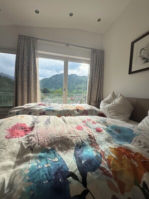 Quarto com cama, cortinas, janela com vista para montanhas e quadro na parede.