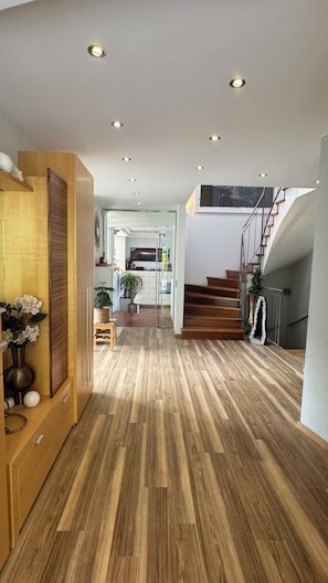 Un intérieur moderne avec un plancher en bois, un escalier et des spots encastrés au plafond.