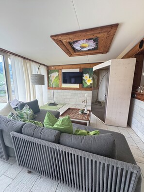 A modern living room with a grey sectional sofa, a wooden coffee table, and a flat-screen TV mounted on a white brick wall. - A dreamy vacation home with a magnificent panoramic view (Sankt Johann im Pongau)