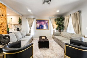 Ein modernes Wohnzimmer mit einem beigen Sofa, einem schwarzen Hocker und einem großen Gemälde an der Wand.