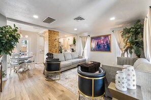 A modern living room with a grey sofa, a dining table with chairs, and a kitchen area in the background. - Fremont House|2 Primary Suites|Private Parking (Las Vegas)