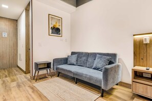 Ein modernes Wohnzimmer mit einem grauen Sofa, einem kleinen Beistelltisch, einem gerahmten Bild an der Wand und einem Holzschrank.
