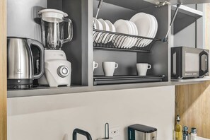 Eine Küche mit Mixer, Wasserkocher, Mikrowelle und Geschirrgestell mit Tellern und Tassen.