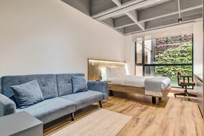 Camera moderna con un divano grigio, un letto in legno e vista sul verde attraverso ampie finestre.