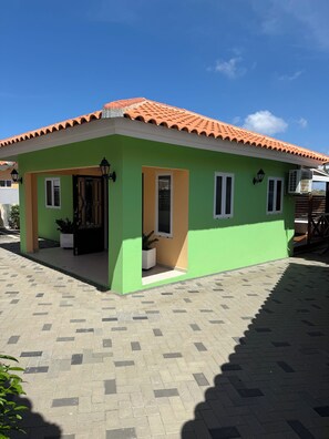 A single-story building with a tiled roof, a green facade, and a paved entrance area.