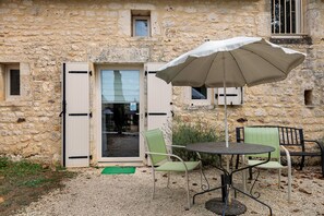 A stone building with a door, a window, and a table with chairs and an umbrella. - Room 'Chambre Lune' with Shared Pool, Wi-Fi and Air Conditioning - Table d'Hôtes (Salignac Eyvigues)