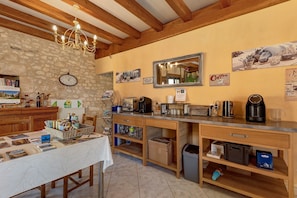 A rustic kitchen with a stone wall, wooden beams, a chandelier, a coffee station, and various kitchen appliances. - Room 'Chambre Lune' with Shared Pool, Wi-Fi and Air Conditioning - Table d'Hôtes (Salignac Eyvigues)