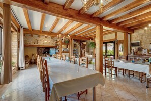 A spacious dining area with a long table, wooden beams, stone walls, and a chandelier. - Room 'Ange' with Shared Pool, Wi-Fi and Air Conditioning (Salignac Eyvigues)