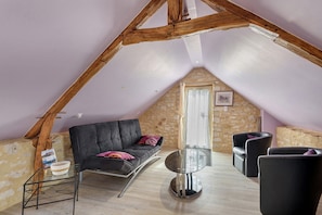 A cozy attic room with a black sofa, a round glass table, and a stone wall. - Room 'Chambre Etoile' with shared pool, Wi-Fi and air conditioning - Table d'Hôte (Salignac Eyvigues)
