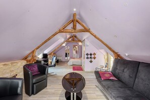 Quarto estilo loft com teto inclinado, cama, sofá e mesa de centro.
