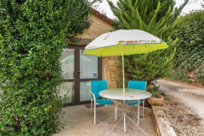 Eine Terrasse mit Tisch und Stühlen unter einem weißen Sonnenschirm, umgeben von Grünpflanzen.