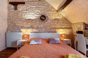 Ein Schlafzimmer mit Steinsturz, einem Bett mit gemusterten Betttextilien, zwei Nachttischlampen, einem Heizkörper und einem Schreibtisch mit Stuhl.