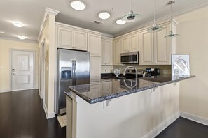 A modern kitchen with a central island, stainless steel appliances, and pendant lighting. - Serene Waterfront Condo with Pool (Biloxi)