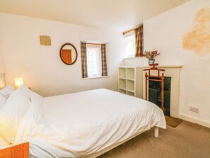 Ein Schlafzimmer mit Bett, Spiegel, einem Fenster mit Vorhängen, einem Kamin und einem Regal mit Blumen.