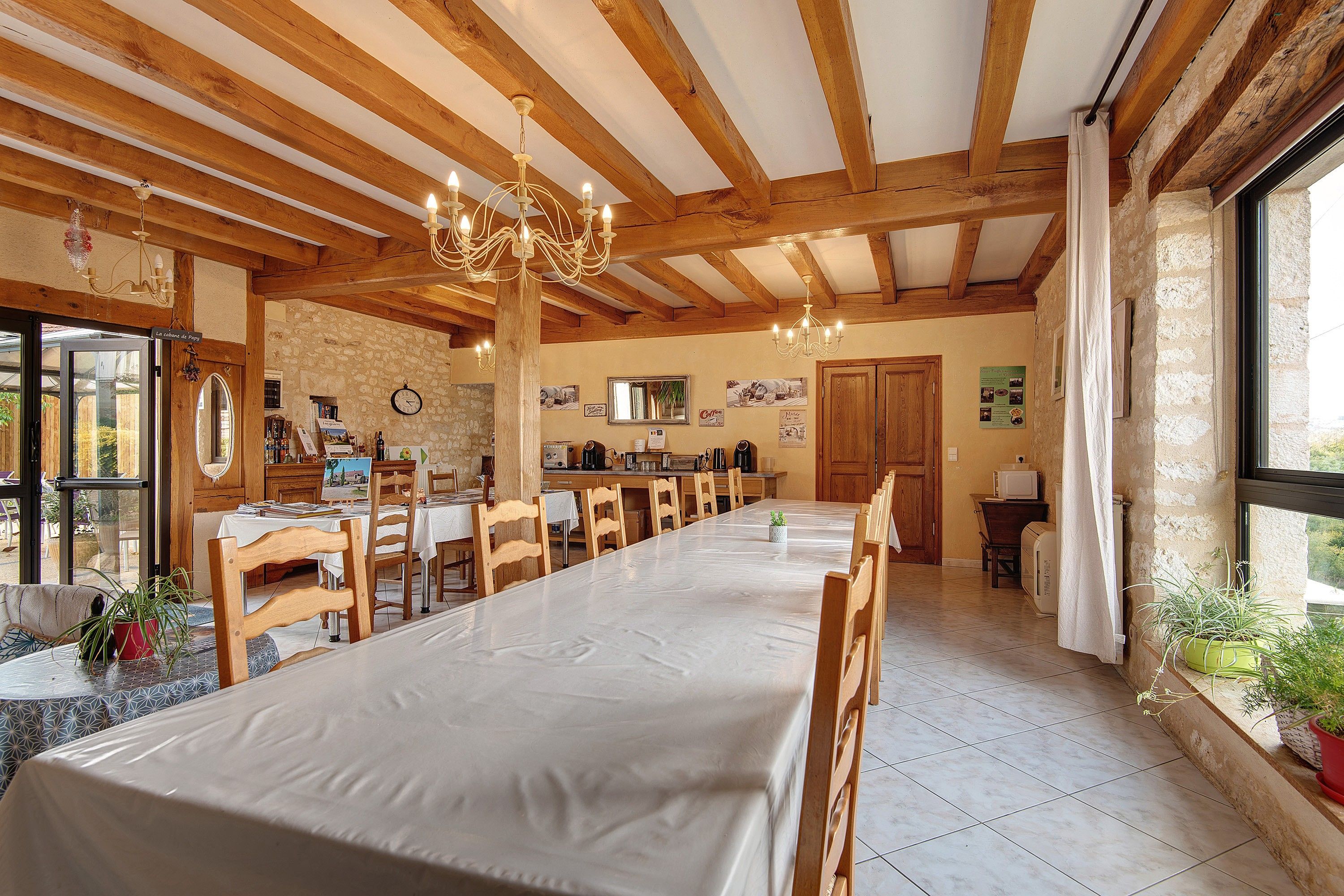 Un espace repas avec une longue table, des chaises en bois, un lustre et un mur en pierre.