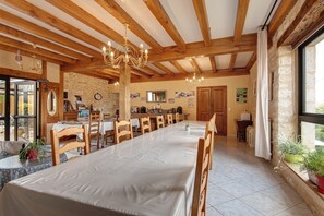 A dining area with a long table, wooden chairs, a chandelier, and a stone wall. - Room 'Chambre Montagne' with shared pool, Wi-Fi and air conditioning - Table d'Hôte (Salignac-Eyvigues)