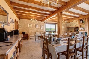 A spacious dining area with wooden beams, a bar area with appliances, and a view through a large window. - Room 'Chambre Romantique' with Shared Pool, Wi-Fi and Air Conditioning - Table d'Hôte (Salignac-Eyvigues)