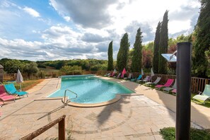 A swimming pool with a stone deck, surrounded by lounge chairs and umbrellas, with tall trees in the background. - Room 'Chambre Romantique' with Shared Pool, Wi-Fi and Air Conditioning - Table d'Hôte (Salignac-Eyvigues)