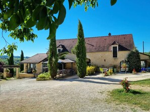 A traditional stone building with a gravel driveway, outdoor seating, and a clear blue sky. - Room 'Chambre Romantique' with Shared Pool, Wi-Fi and Air Conditioning - Table d'Hôte (Salignac-Eyvigues)
