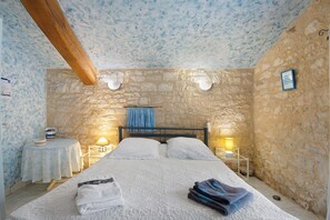 A room with a bed, two bedside tables, a stone wall, and a wooden beam ceiling. - Room 'Chambre Azur' with Shared Pool, Wi-Fi and Air Conditioning (Salignac-Eyvigues)