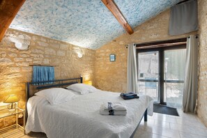 Ein Schlafzimmer mit Steinwand, einem Bett mit weißer Bettwäsche, einem Nachttisch mit Lampe und einem Fenster mit Vorhängen.
