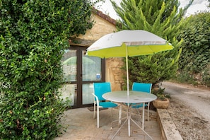 An outdoor seating area with a table and chairs, a white umbrella, and a stone wall. - Room 'Chambre Azur' with Shared Pool, Wi-Fi and Air Conditioning (Salignac-Eyvigues)