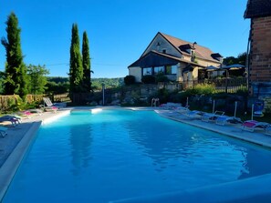 Ein Schwimmbecken mit Liegestühlen, einem Holzzaun und einem Gebäude mit einem geneigten Dach.
