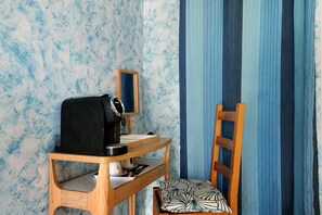 Ein Zimmer mit Schreibtisch aus Holz, einem Stuhl, einer Kaffeemaschine und einem Spiegel an der Wand.