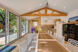 Eine moderne Küche mit Steinwand, Holzbalkendecke und einem großen Esstisch mit weißen Stühlen.