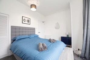 Ein Schlafzimmer mit einem Bett, einem Nachttisch, einem Spiegel und einer Wandleuchte.