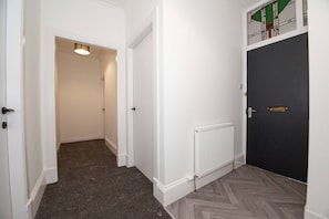 A hallway with carpeted flooring, a radiator, and a dark door with a gold handle. - Vacant Nests 3BR Golf Course Wi-FI (Carnoustie)