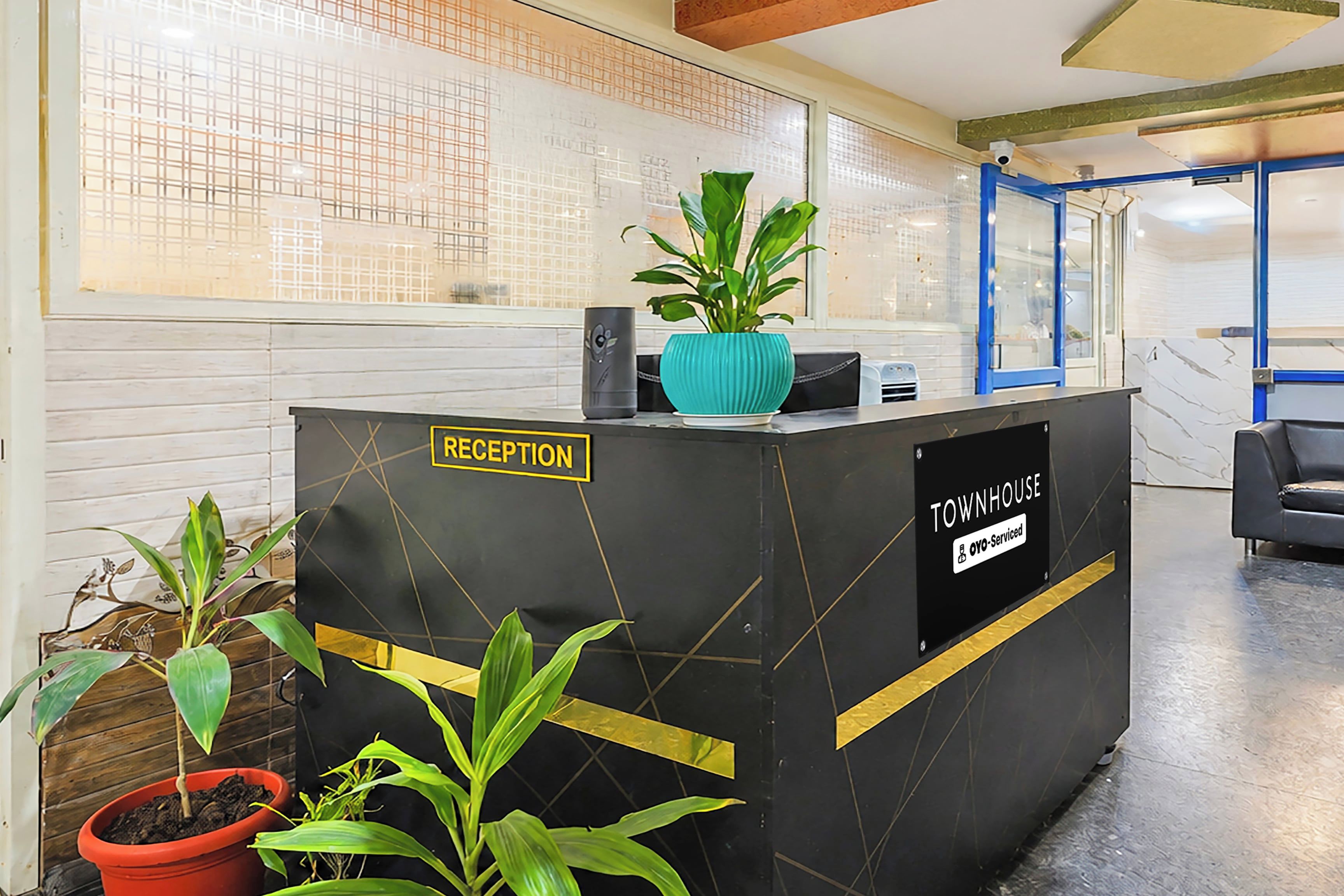 A reception desk with a sign indicating it's the reception area, a blue plant on top, and a sign stating it's serviced by OYO.
