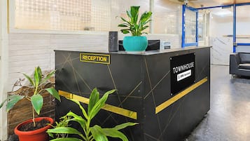 A reception desk with a sign indicating it's the reception area, a blue plant on top, and a sign stating it's serviced by OYO.