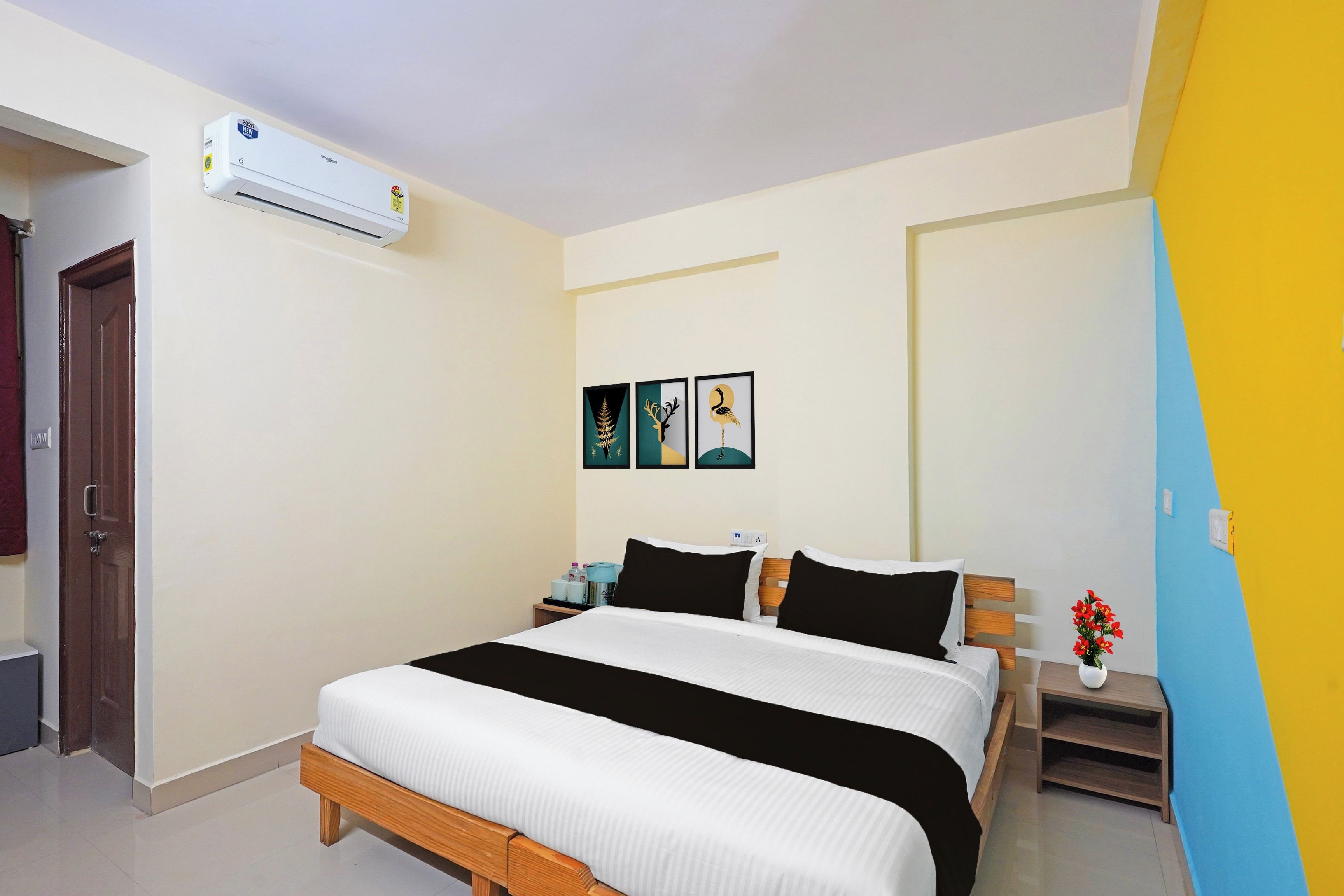 A hotel room with a bed, a nightstand, a wall-mounted air conditioner, and a door.