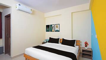 A hotel room with a bed, a nightstand, a wall-mounted air conditioner, and a door.