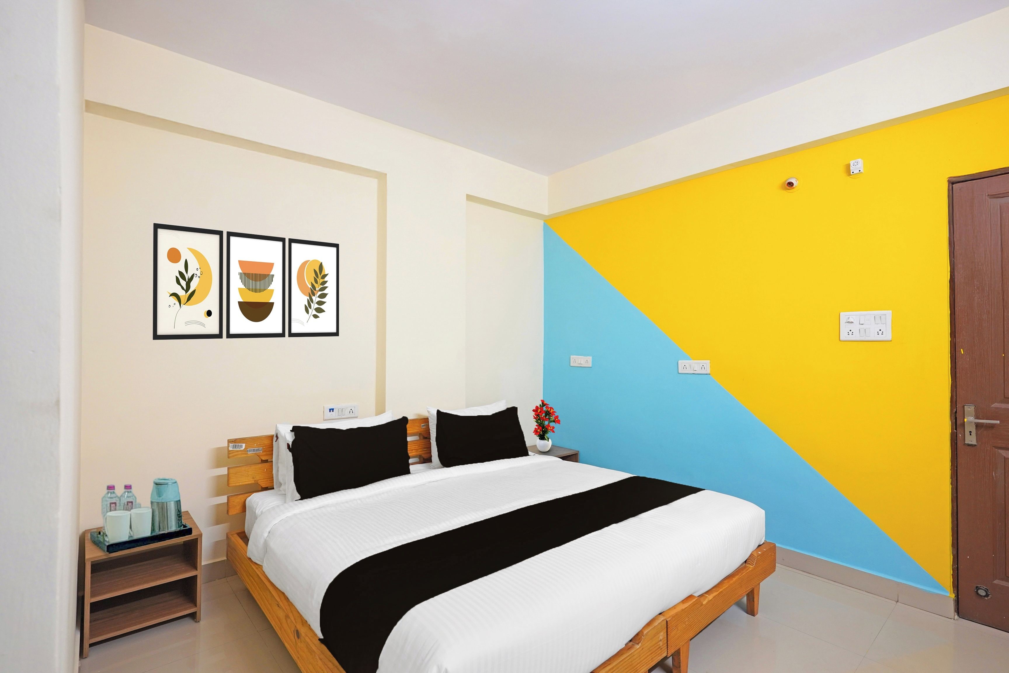 Un dormitorio con cama, mesita de noche, pared con tres cuadros enmarcados y una puerta.