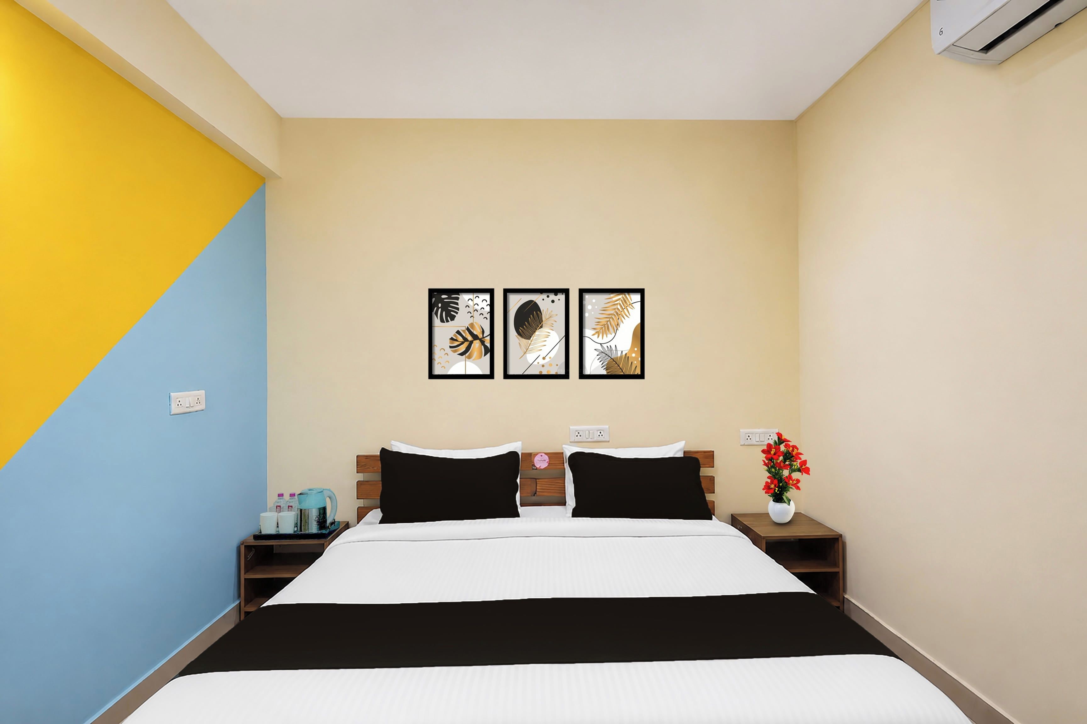 A hotel room with a bed, bedside tables, a nightstand, a wall-mounted air conditioner, and three framed artworks on the wall.