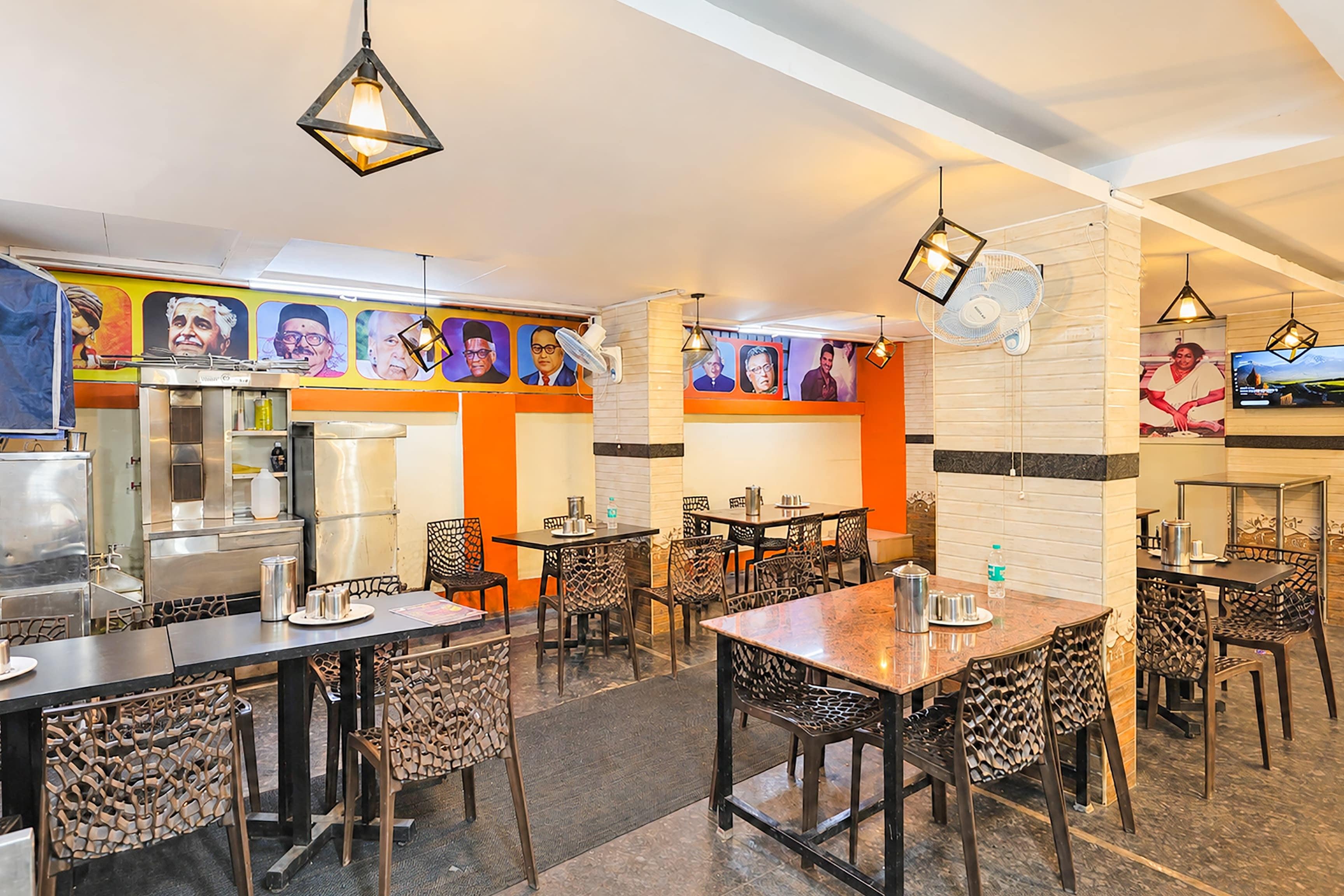A restaurant with multiple dining tables and chairs, a kitchen area, and wall-mounted fans.