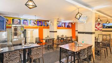 A restaurant with multiple dining tables and chairs, a kitchen area, and wall-mounted fans.