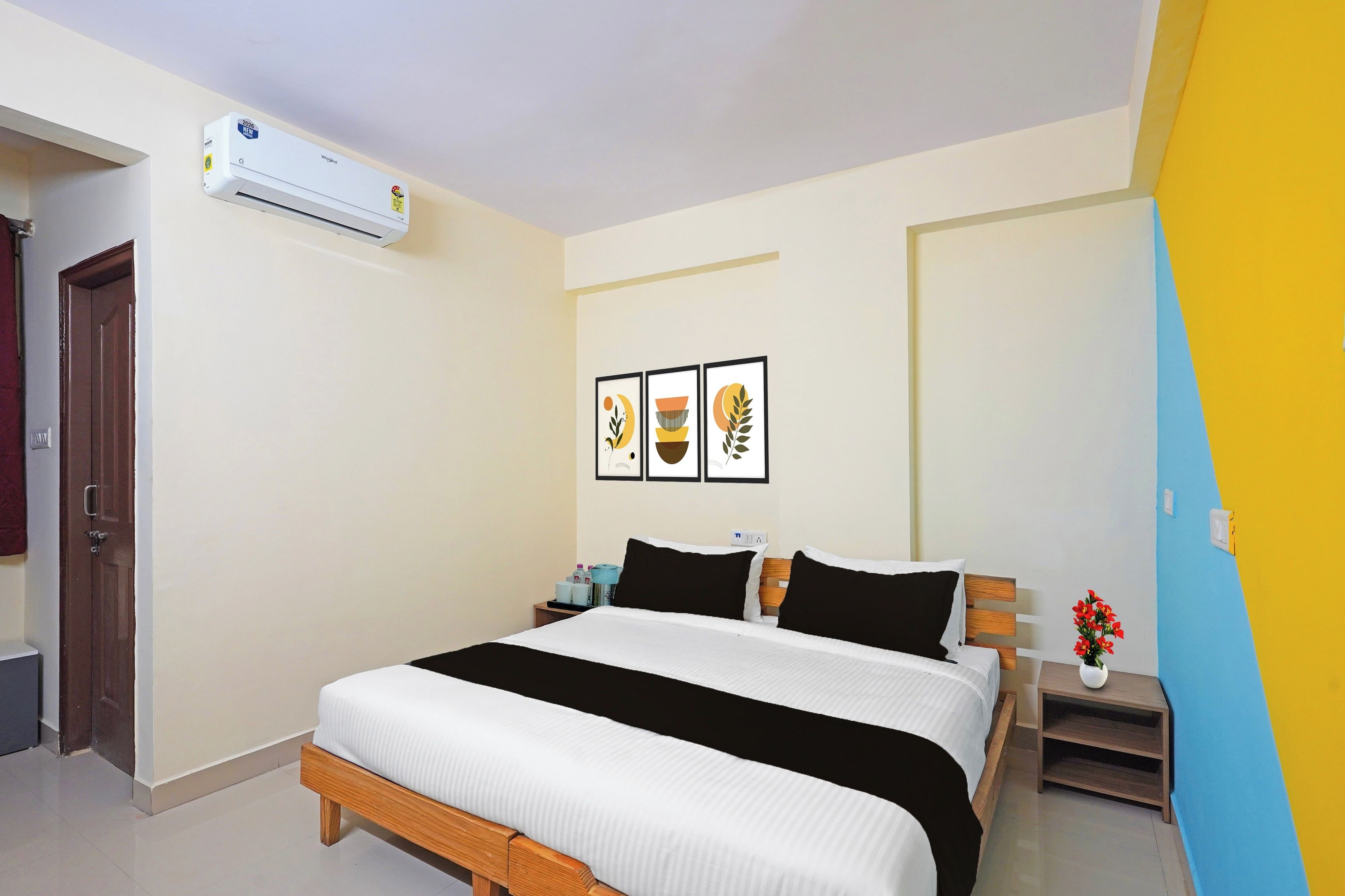 Una habitación de hotel con cama, mesitas de noche, aire acondicionado de pared y cuadros enmarcados.