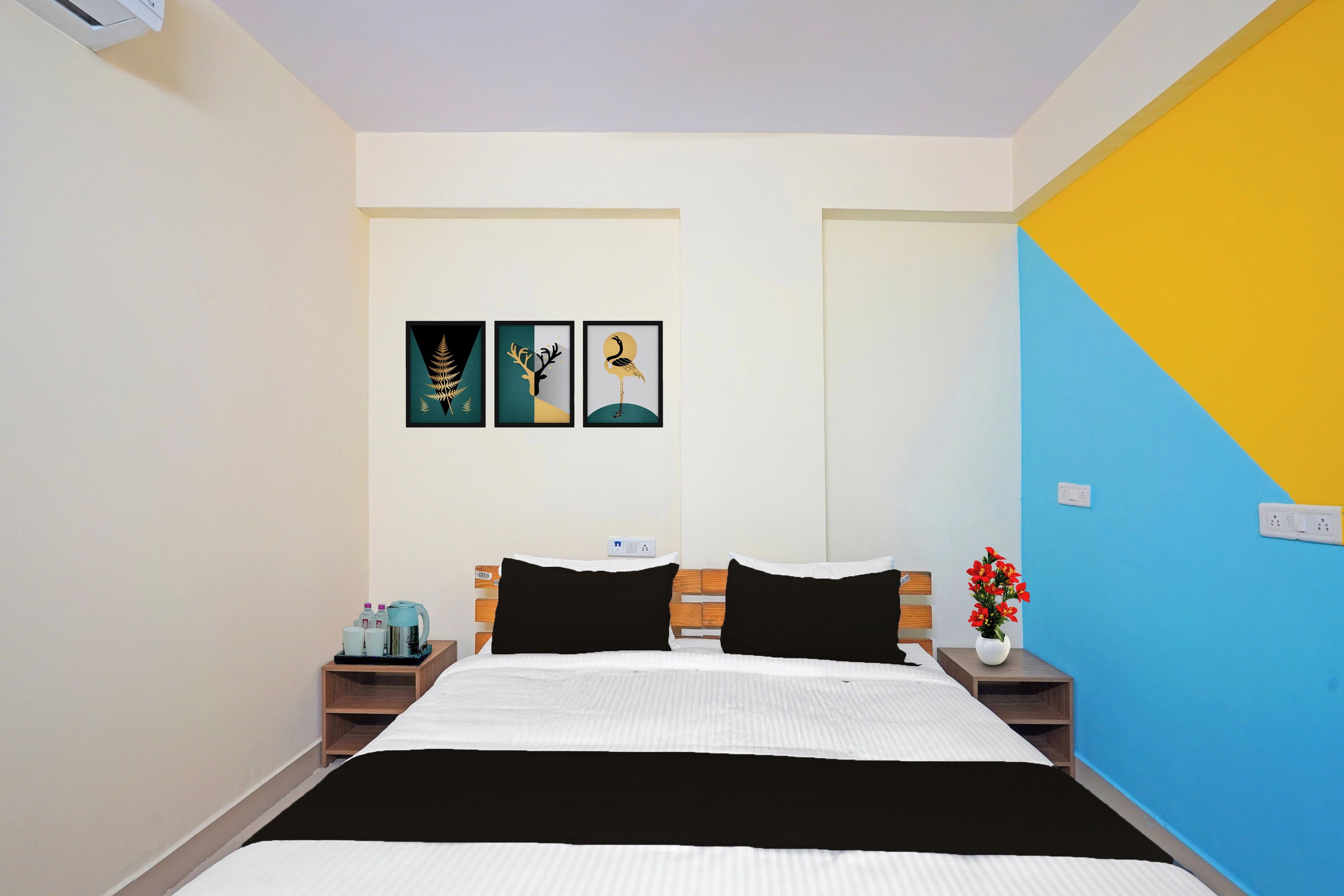 A hotel room with a bed, two nightstands, a coffee maker, a vase with flowers, and three framed pictures on the wall.