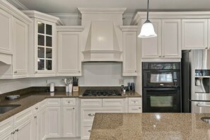 A kitchen with white cabinetry, a stainless steel refrigerator, a built-in oven, and a granite countertop. - War Eagle Manor:Your Auburn Getaway (Auburn)