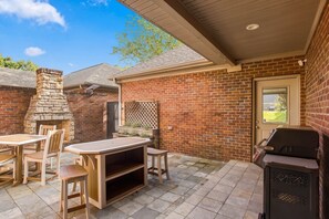 A patio area with a brick wall, a stone fireplace, a grill, and a table with chairs. - War Eagle Manor:Your Auburn Getaway (Auburn)